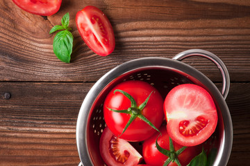 Tomatoes with basil in colander on wooden table background. Food composition. Top view