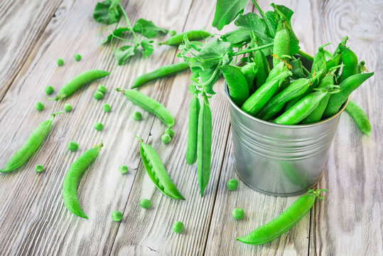 Green pea pods in a tin on wooden table
