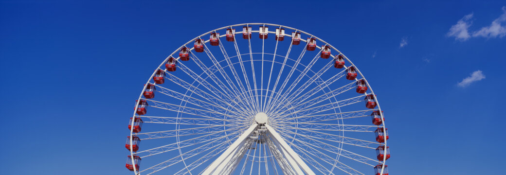This is an aerial view of the giant Ferris wheel at Navy Pier during summer. It is a view of half the Ferris wheel against a blue sky.