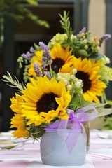 Objects: Sunflowers in a flower arrangement with a bow on a table with napkins, silverware and balloons in the background.