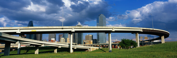 Fototapeta na wymiar This is a freeway overpass with the Dallas skyline visible behind it. The freeway curves and snakes around in a circle in front of the city.