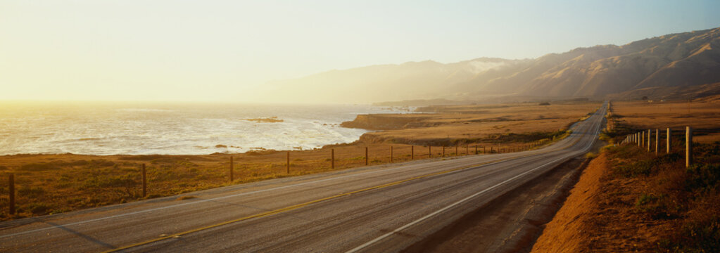 This is Route 1also known as the Pacific Coast Highway. The road is situated next to the ocean with the mountains in the distance. The road goes off into infinity into the sunset.