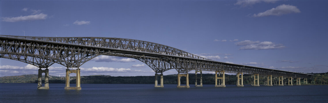 This is the Beacon Bridge which is over the Hudson River. It is a large steel bridge. The water and sky are blue.