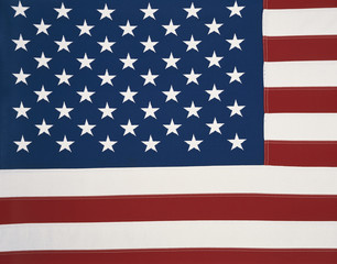 This is an American flag sitting flat. We see all of the stars on the blue background with the red and white stripes also laying flat moving in a straight horizontal direction, but not completely shown.