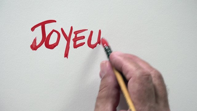 Human hand writing word "JOYEUX ANNIVERSAIRE" in french, with red gouache