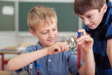 kinder in der schule schauen mit einer lupe auf ein reagenzglas