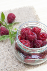 Fresh sweet red raspberry in a glass jar and mint on light wooden table, selective focus