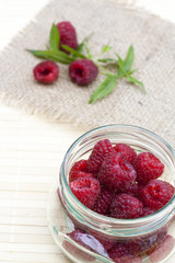 Fresh sweet red raspberry in a glass jar and mint on light wooden table, selective focus