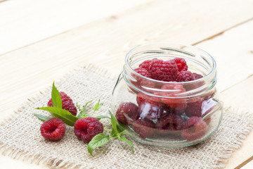 Fresh sweet red raspberry in a glass jar and mint on light wooden table, selective focus