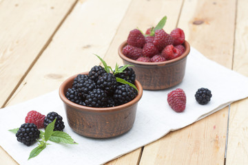 Fresh sweet red raspberry and blueberries in a clay pot and mint on light wooden table, selective focus