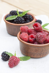 Fresh sweet red raspberry and blueberries in a clay pot and mint on light wooden table, selective focus