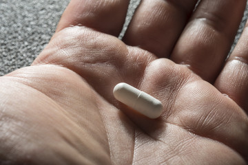 Bare hand holding one white medicinal tablet
