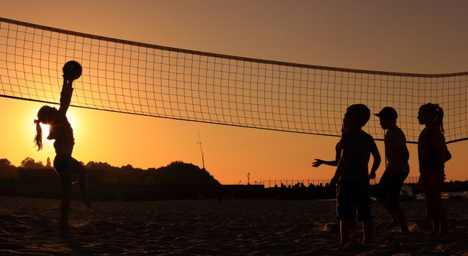 Children playing on the beach volleyball at sunset