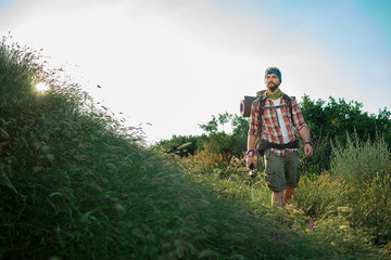 Young caucasian man with backpack walking on a green meadow