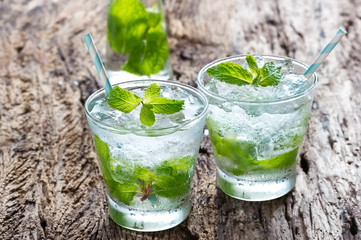 glass of cold water with fresh mint leaves and ice cubes on wood