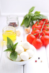 red tomatoes, garlic, basil and mozzarella cheese on a white wooden background