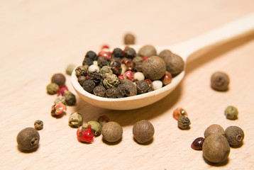 Spoon filled with grains of pepper  on a wooden surface