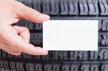 Hand holding blank card on car wheel tire background