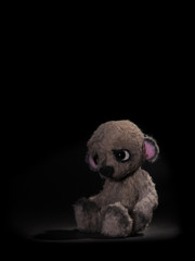 Cute sad little teddy bear alone on a black background