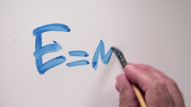 Human hand writing word "E=MC2" with blue gouache