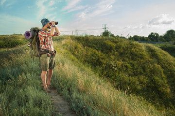 Young caucasian man with backpack standing on the top of hill