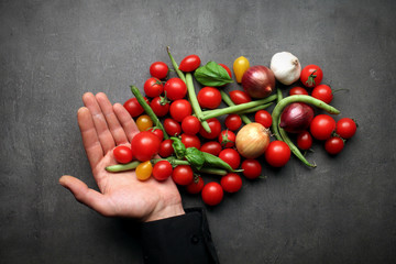 Hand with fresh vegetables on grey kitchen table background