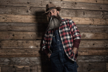 Smoking vintage worker man with long gray beard in jeans dungare