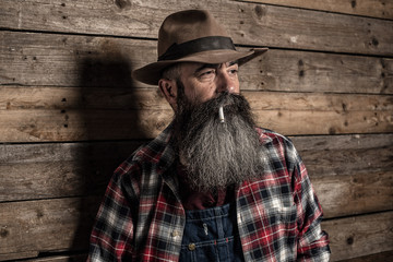 Smoking vintage worker man with long gray beard in jeans dungare