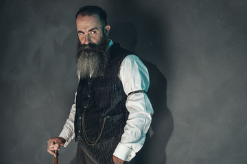 Vintage beard man in 1900 style fashion with cane against grey w