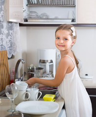 female child cleaning dishware at home