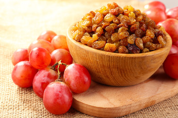 Raisins in bowl with grapes on table close up