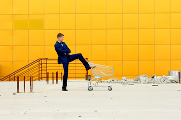 A man in a blue suit with an empty  shopping  cart outdoors.