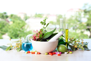 Herbs in mortar, test tubes and pills,  on table, on bright background