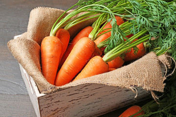 Fresh organic carrots in box with sackcloth on wooden table, closeup