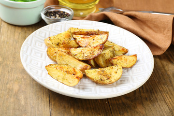 Baked spicy potatoes in white plate on wooden table, closeup