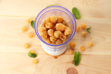 Yellow raspberries in blender cup on wooden table, closeup