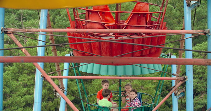 Four kids pointing at camera as they riding a Ferris wheel 
