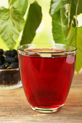 Glass of refreshing mulberry juice with berries on table close up