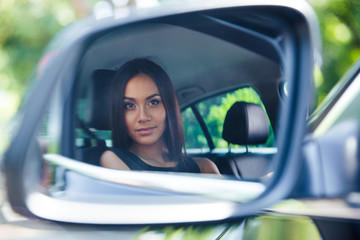 Woman looking at her reflection in a car mirror