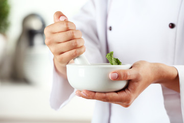 Cook hands with mortar with herbs on bright background