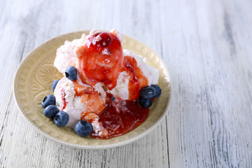 Delicious ice cream with fresh frozen berries and sauce, on color wooden background