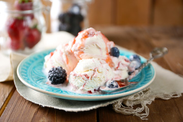 Delicious ice cream with fresh frozen berries and sauce, on wooden background
