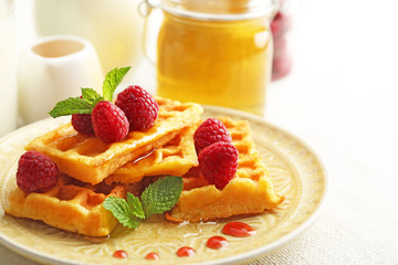 Sweet homemade waffles with fresh raspberries on plate, on light background