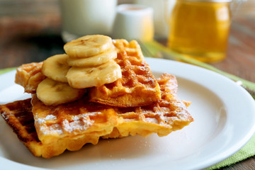 Sweet homemade waffles with sliced banana on plate, on light background