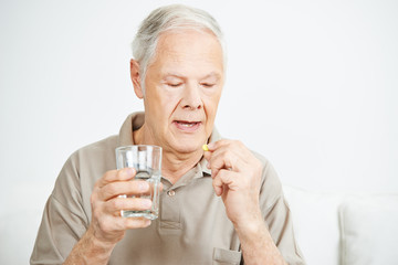 Senior schluckt Tablette mit Wasser