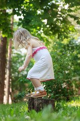 Naklejka na ściany i meble Toddler girl jumping down from tree stump back view