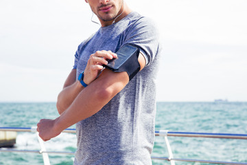 Male runner listening to music adjusting settings on armband for smartphone