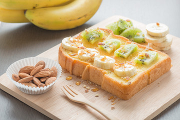 Toast topped with banana ,kiwi, almonds and honey on the wooden
