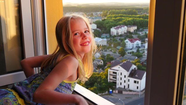 Small girl looks down threw the window and waves hello in sunny day