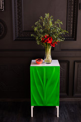 Fototapeta na wymiar Bouquet of red calla lilies in a glass vase with a pomegranate and eucalyptus stands on the bedside table on a black background 